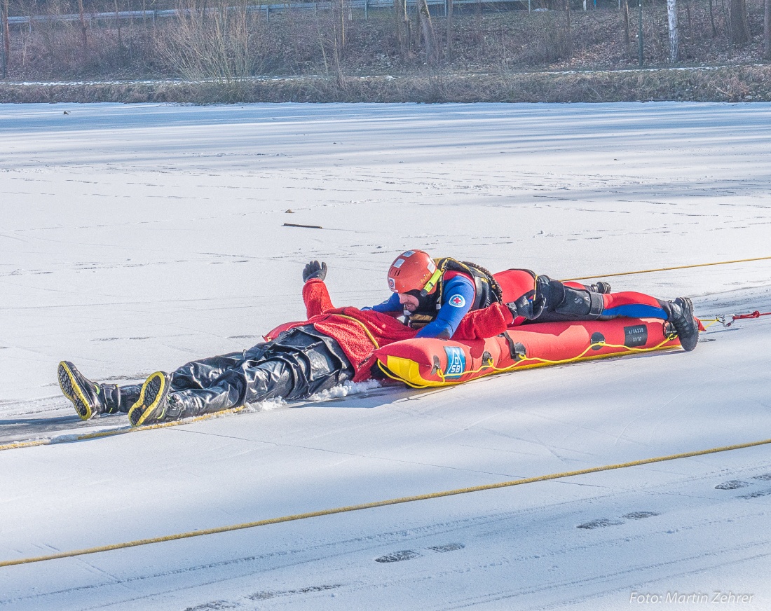 Foto: Martin Zehrer - Hier kann man gut erkennen:<br />
Die im Eis eingebrochene Person ist aus dem Wasser befreit und wird von dem Rettungs-Helfer auf einer Art Schlitten von der Gefahrenstelle en 